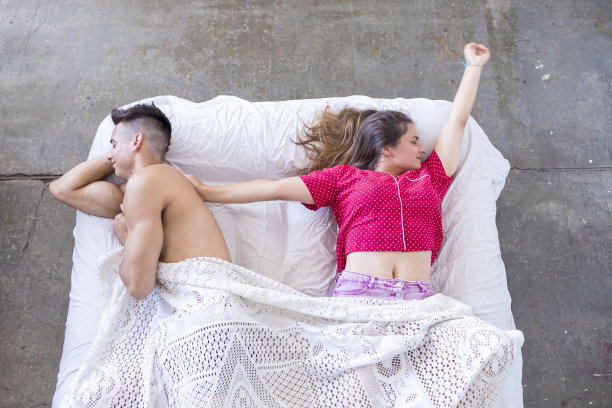 深色头发的女性在睡好觉后躺在床上伸懒腰，而丈夫正在睡觉图片下载