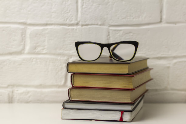 桌子上放着一叠要读或研究的书和眼镜。图片下载