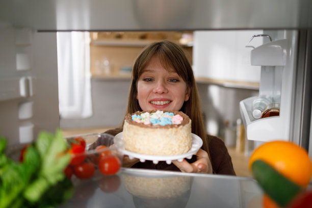 兴高采烈的年轻女子从冰箱里拿出一块美味的蛋糕图片下载