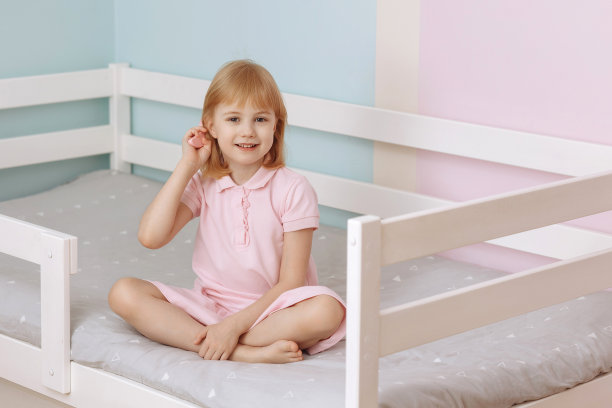 一个学龄前的小女孩穿着粉红色的裙子坐在床上梳头发。图片下载