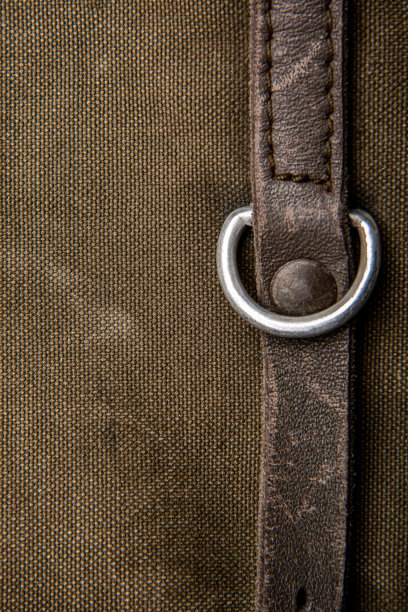 特写帆布织物背包的纹理。皮革带和金属扣。的卡其色背景。图片下载