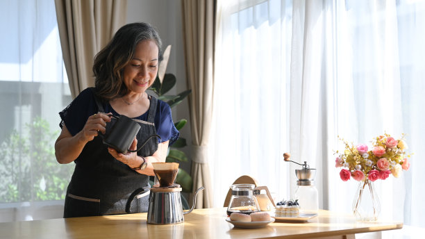 积极的中年人站在厨房的桌子上，煮着滴滤咖啡，享受着她的早晨。图片下载