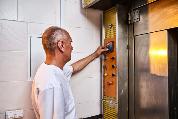 专业的面包师穿着统一的服装，在面包房的工业烤箱中放入烤生面团的面板图片下载