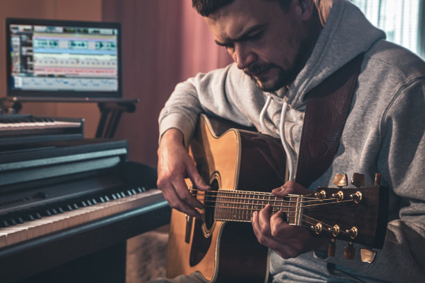 男音乐家在家工作，在电脑旁边弹吉他。图片下载