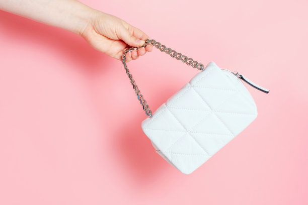 女性手里拿着一个白色的包与铁带在粉红色的背景特写。图片下载