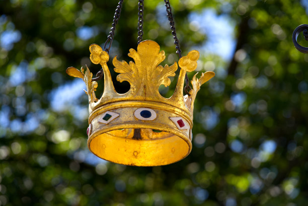 在一个阳光明媚的夏日，广东Zürich, Forch村餐厅外挂着金色的皇冠，背景是散焦的树。图片下载