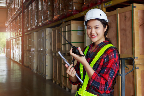 仓储物流管理业务;年轻的亚洲女性穿着反光安全背心和白色头盔;在仓库工厂通过对讲机进行沟通图片下载