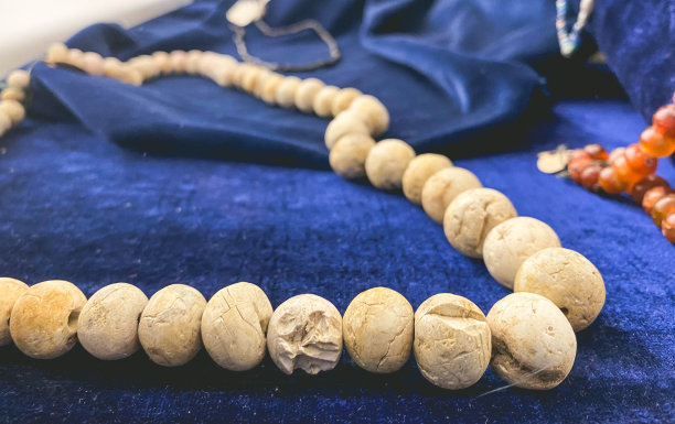 蓝色天鹅绒衬垫上用石头做成的珠子。在基座上的博物馆展览。有破损的古代珠宝图片下载