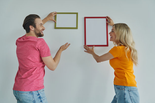 欢快的年轻夫妇在墙上挂着相框，微笑着图片下载