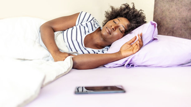 一个年轻女子在床上醒来，查看她的智能手机。女人在床上醒来立刻伸手看手机。图片下载