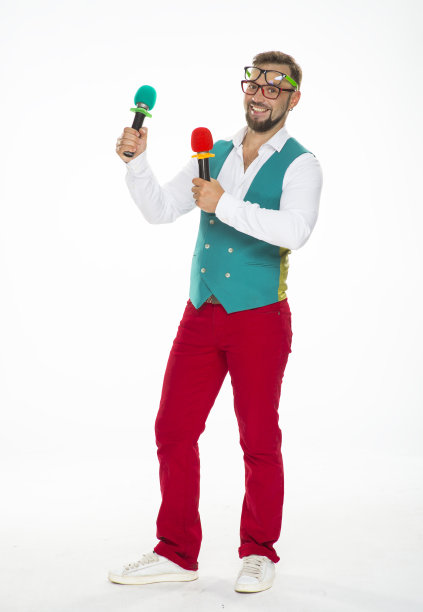 拿麦克风的人在笑。一个兴高采烈的家伙，手里拿着两个麦克风，脸上戴着两副眼镜，穿着红色裤子和背心，在一个孤立的白色背景上滑稽地摆着姿势图片下载