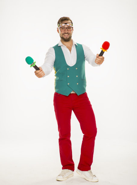 拿麦克风的人在笑。一个兴高采烈的家伙，手里拿着两个麦克风，脸上戴着两副眼镜，穿着红色裤子和背心，在一个孤立的白色背景上滑稽地摆着姿势图片下载