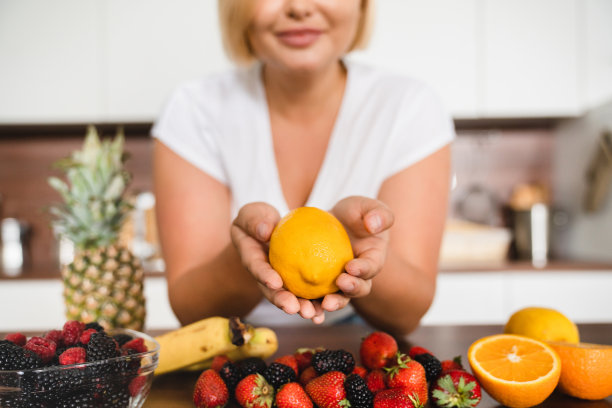 特写照片，年轻的大尺寸丰满的女人拿着橙子，各种水果和蔬菜站在家里的厨房。准备食物，健康饮食图片下载