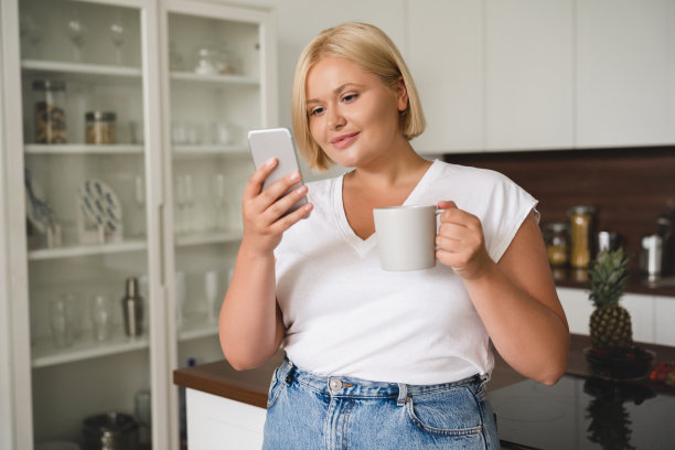 在厨房用智能手机、喝着茶喝着咖啡吃着早餐、在社交媒体(sns)上发帖、在线学习、电子商务的白人自由职业女性图片下载