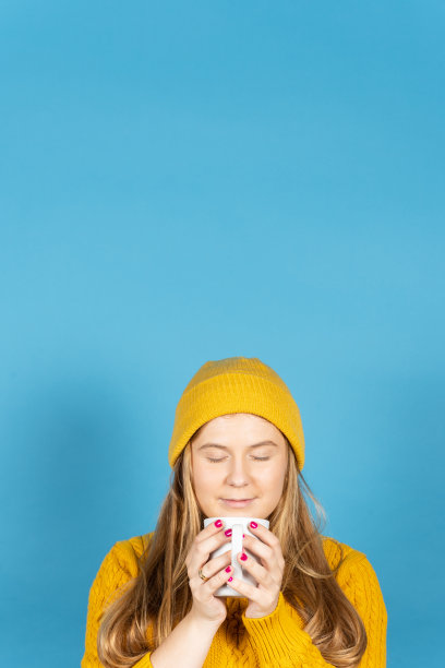 北欧年轻女子在蓝色背景下闻咖啡。图片下载