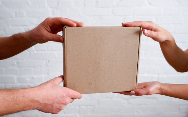 交付。快递员把纸板箱递给女人。特写镜头在手中。白砖墙背景。图片下载