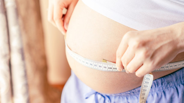 孕妇测肚子。幸福美丽的孕妇用卷尺量肚子。孕、药保健理念。图片下载