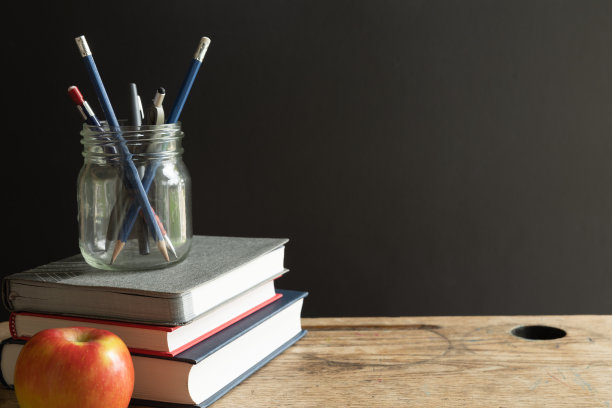 书，一罐钢笔和红苹果在黑色背景的复古书桌图片下载