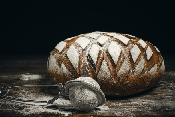 在黑麦面包上撒上面粉，用筛子筛撒在黑色背景上。图片下载