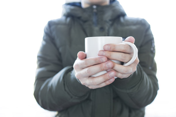 一个人在寒冷的天气里拿着一个白色的杯子。图片下载
