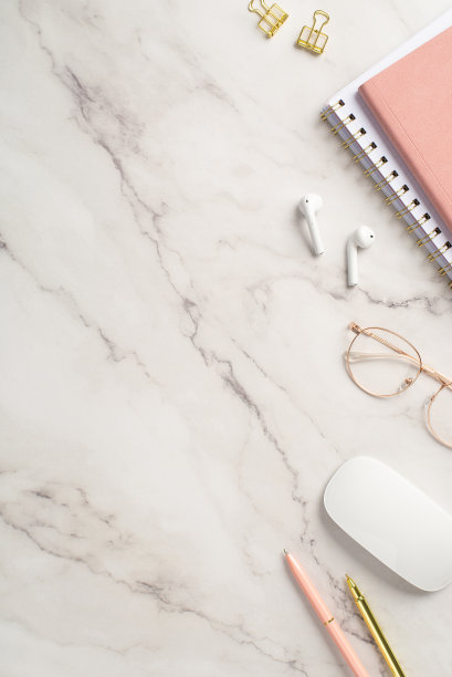 经营理念。俯视图垂直的工作站的照片，粉红色的记事本笔，金色的活页夹，电脑鼠标，无线耳机和时髦的眼镜在白色大理石的背景图片下载