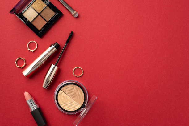 化妆美容概念。顶视图照片的口红轮廓眼影调色板金戒指睫毛膏和化妆刷上孤立的红色背景与copyspace图片下载