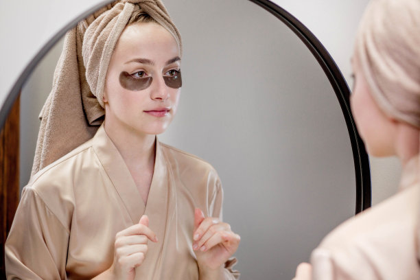 年轻女子在米色毛巾和浴袍，照顾皮肤下的眼睛与补丁。图片下载