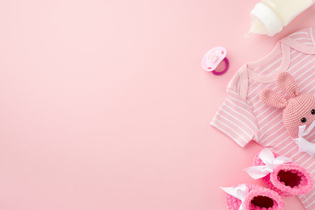小配件的概念。俯视图照片的粉红色婴儿衣服紧身衣靴子婴儿的假瓶和针织兔拨浪鼓玩具孤立粉彩粉红色的背景与空白图片下载