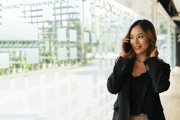 亚洲女人与智能手机站在街道模糊的建筑背景，时尚商业照片美丽的女孩在休闲套房与智能手机。图片下载