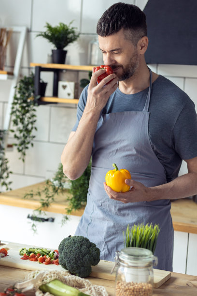 英俊的父亲，强壮的年轻人用新鲜的有机食材烹饪健康的蔬菜沙拉，在家里的厨房里美味的食物。男人做家务。成熟的辣椒，番茄，黄瓜图片下载
