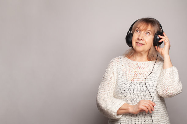 快乐迷人的年长女性微笑放松地听音乐与耳机，看着白色工作室的墙壁背景图片下载