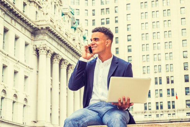 年轻人在笔记本电脑上工作，打电话，坐在纽约的办公楼外面图片下载