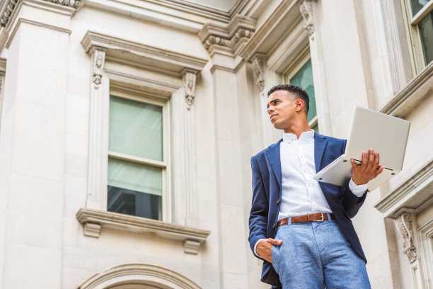 一个年轻人在笔记本电脑前工作，站在纽约市的办公楼外图片下载