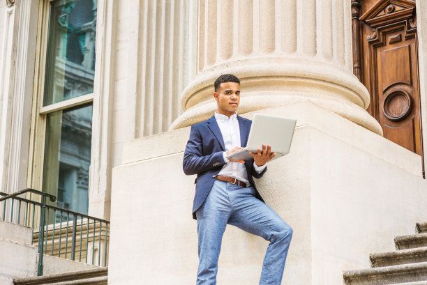 一个年轻人在笔记本电脑前工作，站在纽约市的办公楼外图片下载
