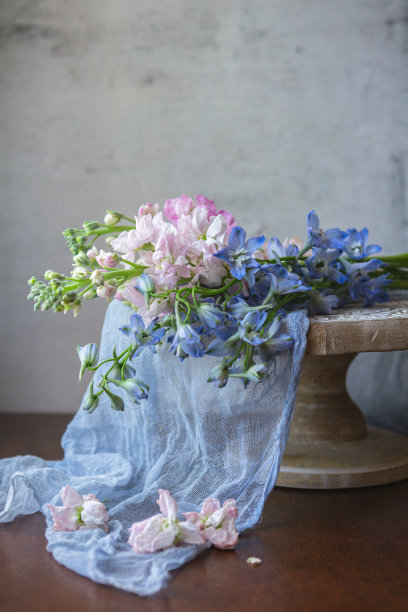 花束的粉红色股票，蓝色风铃花，和金丝桃浆果在一个白色底座，蓝色织物，木桌子，灰色背景图片下载