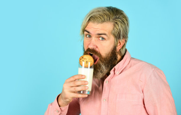 胡子男人喝有用的牛奶配糕点。健康饮食的概念。早餐或午餐食用有机农产品。牛奶和饼干。快乐的农民吃着饼干甜点图片下载