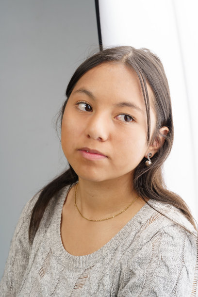 面对一位黑发拉丁年轻女子，身穿灰色呢大衣，自然的美与休闲的风格在工作室图片下载