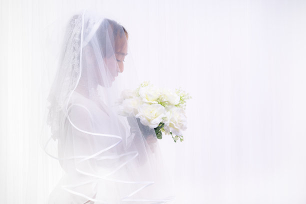 新娘身穿白色礼服，面纱手持花束图片下载