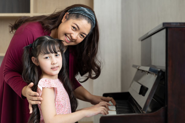 可爱的小女孩和妈妈在家里的客厅里一起弹钢琴。亚洲钢琴家老师在学校教小女孩孩子弹钢琴。图片下载