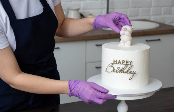 戴着手套的手把巧克力熊放在现成的蛋糕上，上面写着“生日快乐”。有工具和糖果。有选择性的重点。关于糖果商、食物、爱好的照片。图片下载