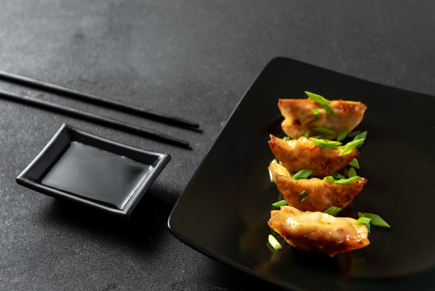 日式煎饺在黑色混凝土背景下的黑色盘子里煎饺子。日本的葱炒饺子图片下载