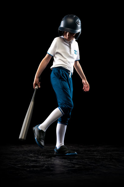 一个穿着蓝白色制服的小棒球手，独自在黑色的演播室背景下玩棒球。体育概念，成绩，学习，竞争图片下载