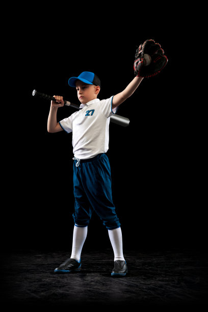小棒球运动员穿着蓝白色的制服在黑色的演播室背景上训练。体育概念，成绩，学习，竞争图片下载