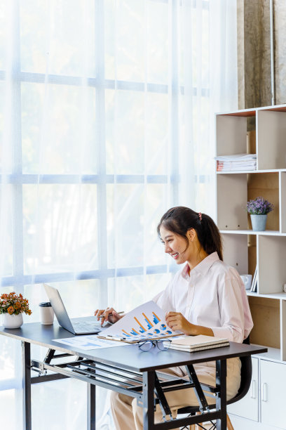 美丽的亚洲女人愉快地在她的办公桌在办公室工作。图片下载