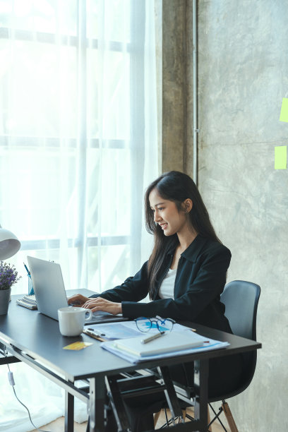 年轻的创意亚洲女性放松使用科技笔记本电脑而坐在桌子上。图片下载