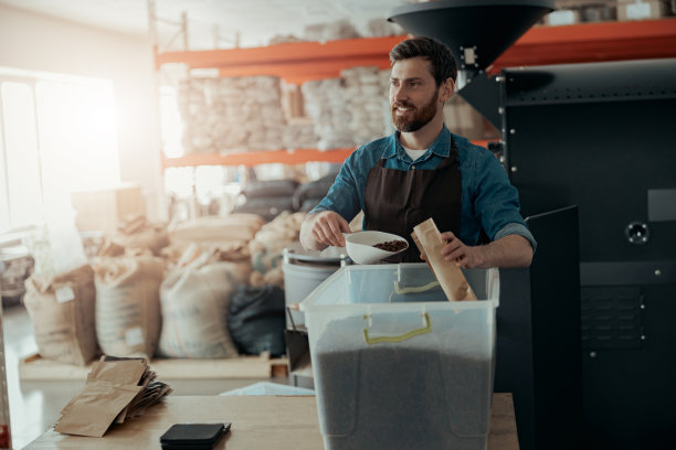 穿着制服的工人把烘焙好的咖啡豆打包出售，然后看向别处图片下载
