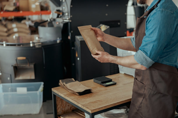 一名男工人在咖啡工厂用秤称装着咖啡豆的纸袋图片下载