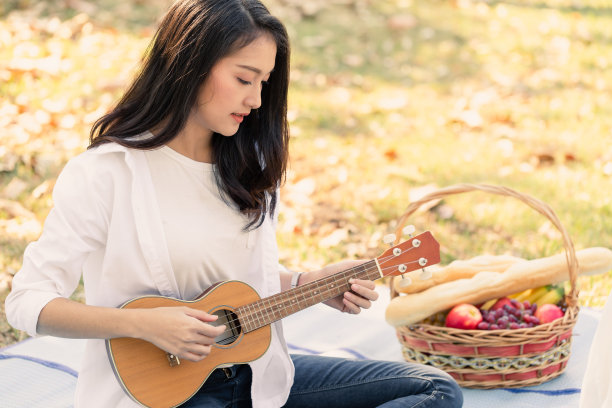 快乐的年轻迷人的亚洲女人玩尤克里里唱歌在公园花园在暑假旅行假期图片下载