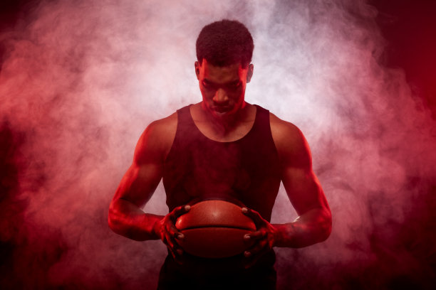 篮球运动员一边点燃与红色拿着一个球对烟雾背景。严重的集中的非洲裔美国人…图片下载
