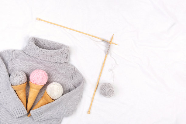 灰色针织毛衣，木制针织针和白色背景纱冰淇淋筒。编织，爱好和手工创作概念。俯视图平铺复制空间图片下载